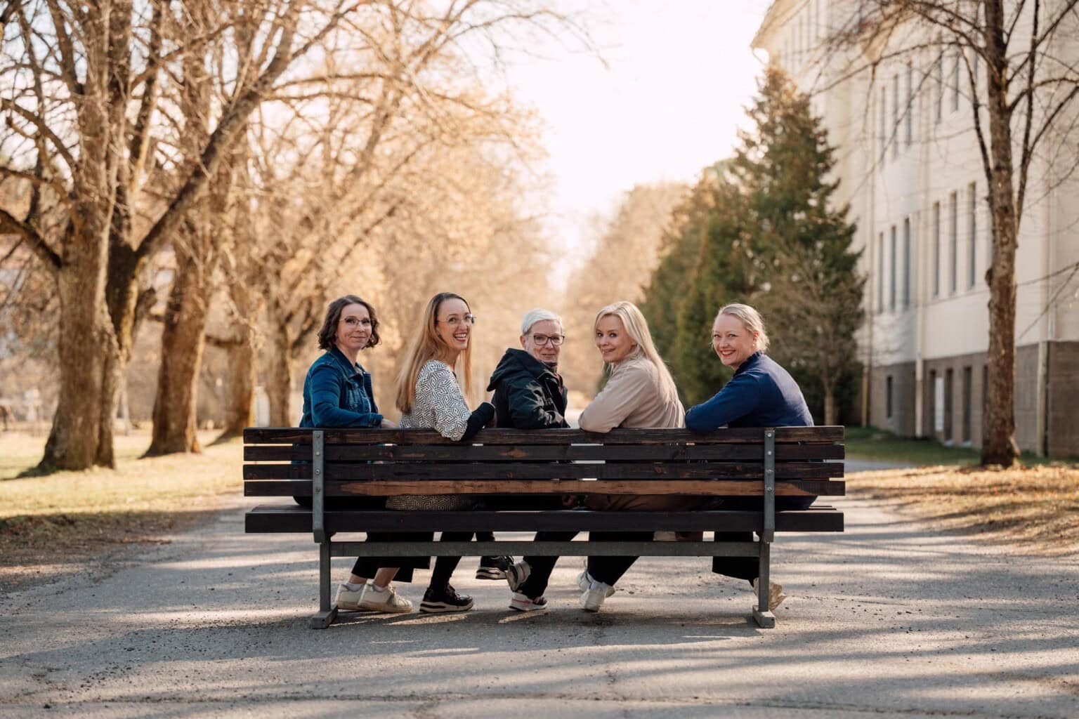 Mielen hyvinvointiin erikoistuneet Mind Teamin ammattilaiset istumassa puiston penkillä kasvot kohti kameraa